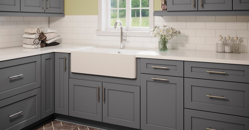 Gray kitchen cabinets with a white farmhouse sink in an open kitchen layout.