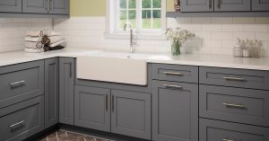 Gray kitchen cabinets with a white farmhouse sink in an open kitchen layout.