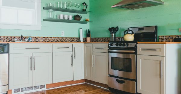 Gray kitchen cabinets with a green tile backsplash and floating shelves.