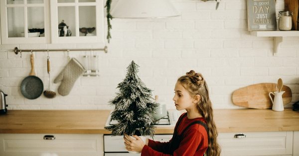 Girl walking through kitchen with holiday tree.