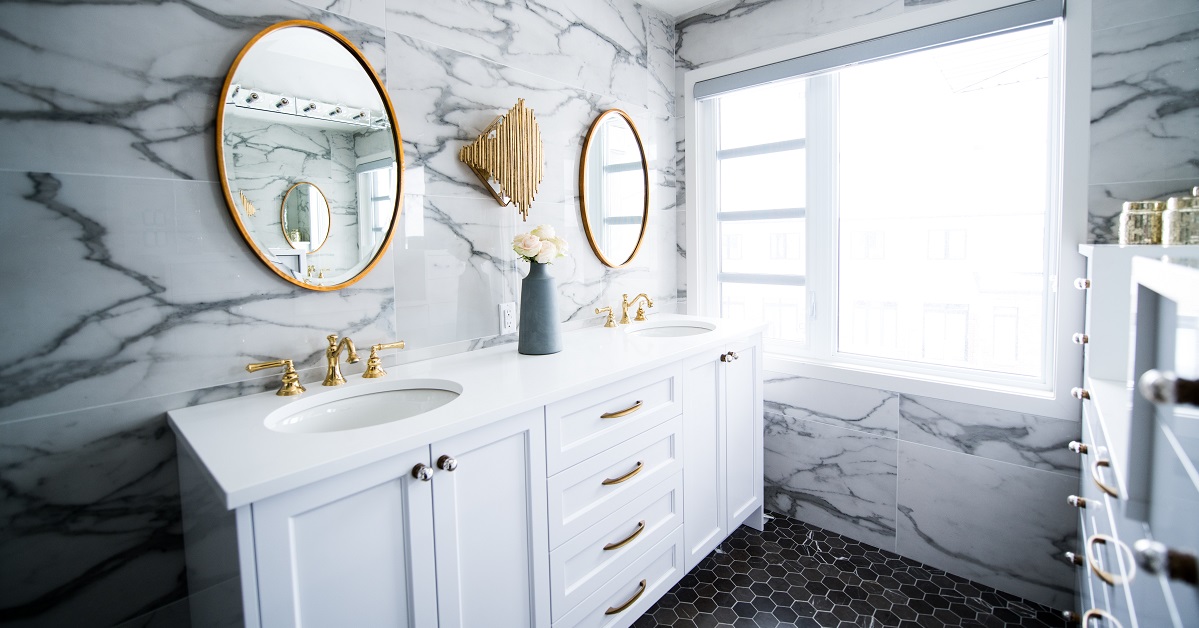 White double vanity with marble wall and large mirrors.