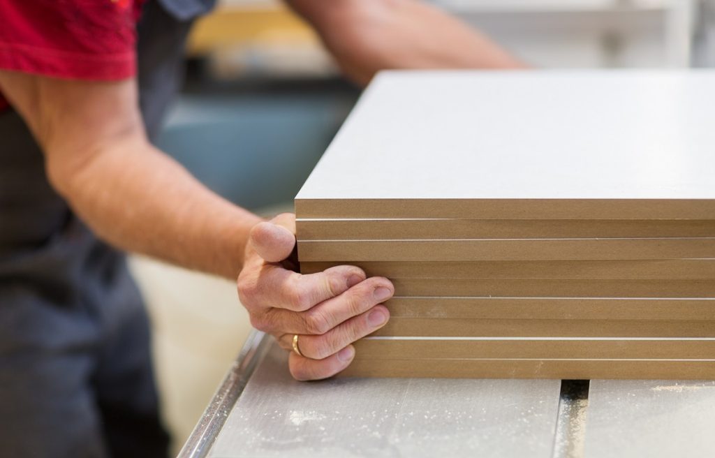 Pieces of unassembled MDF cabinets being stacked by a person.