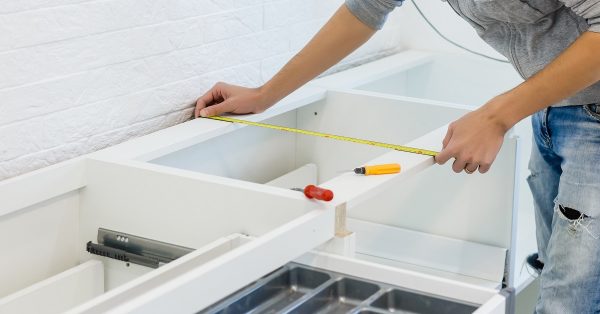Person measuring kitchen cabinets to install.