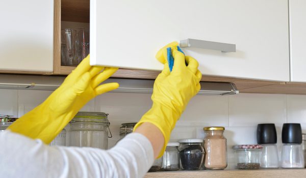 Person wearing yellow gloves cleaning cabinets.