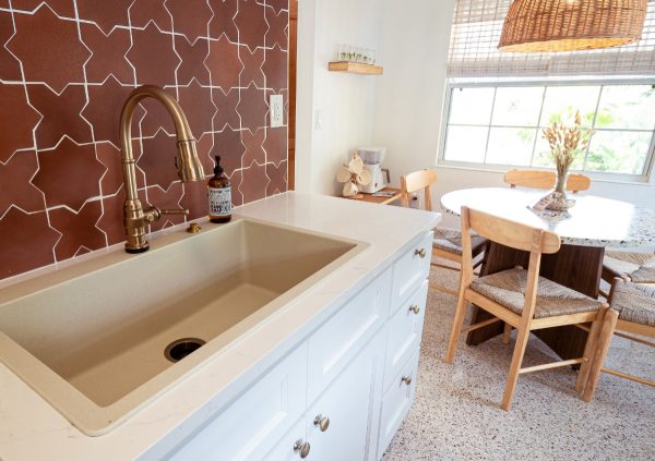 Kitchen with white trough sink, bronze faucet, and terra cotta tile backsplash.