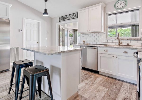 White kitchen with light wood floors and natural stone countertops.
