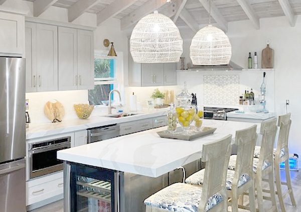 White kitchen with shaker cabinets and island with wicker pendant lights overhead.