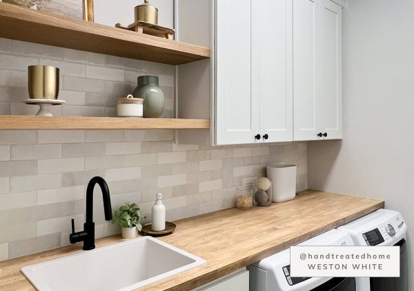 Laundry room with white shaker cabinets, black fixtures, and gray tiled backsplash.