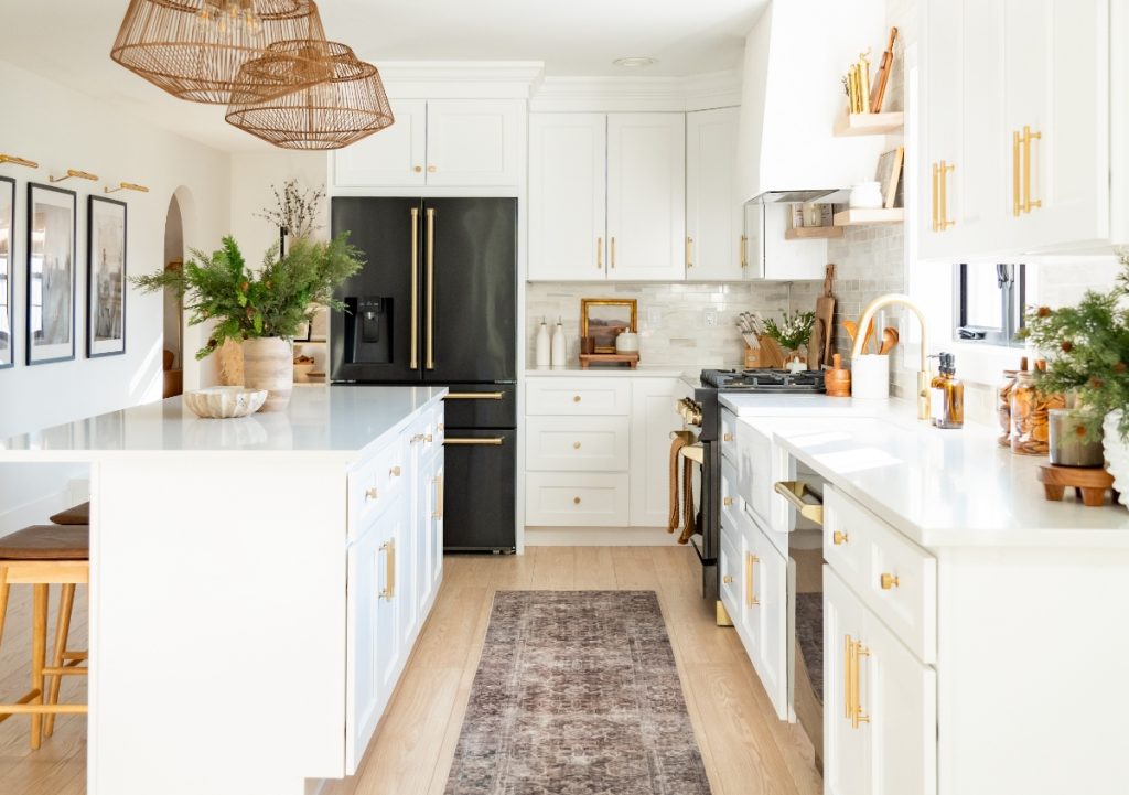Galley kitchen with white cabinets and black appliances with gold hardware.
