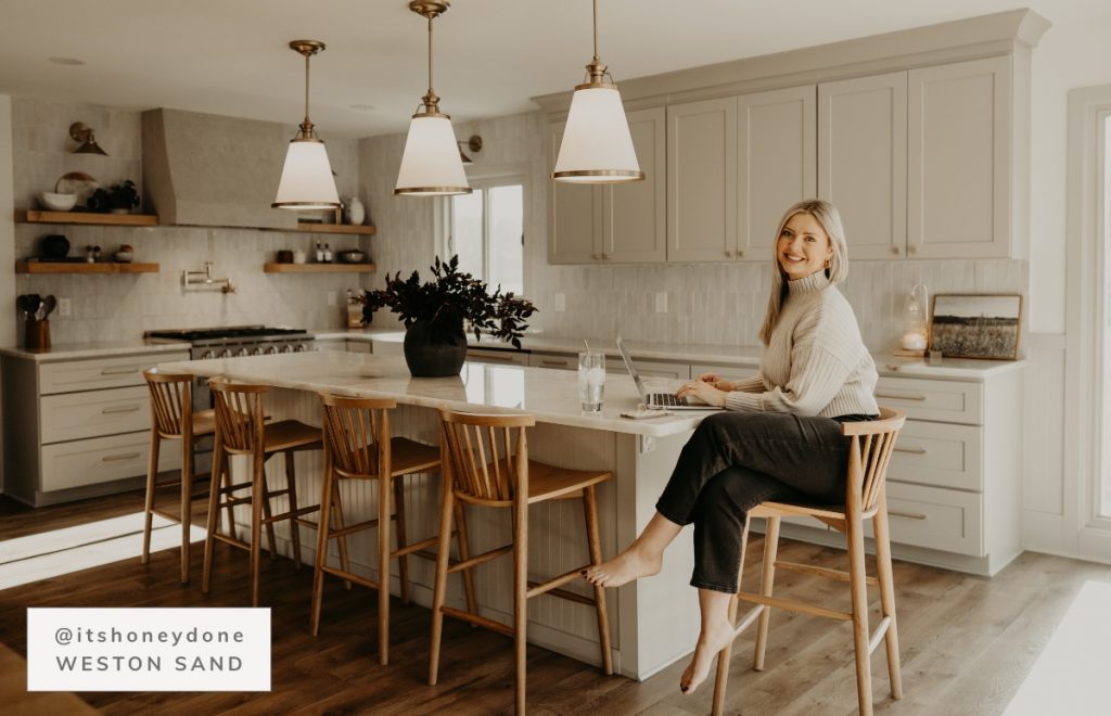 Large kitchen with greige cabinets and large island with statement lighting overhead.