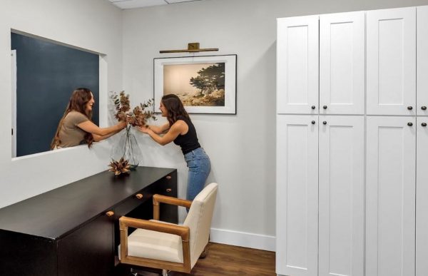 Person decorating a home office space with pantry cabinet in the corner and black desk.