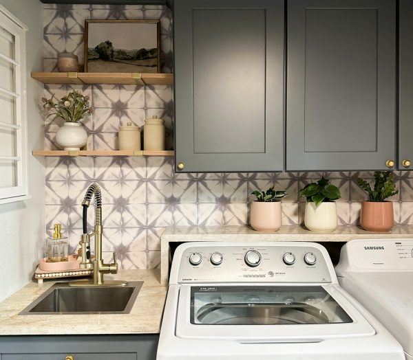 Laundry room with gray cabinets and patterned wallpaper.